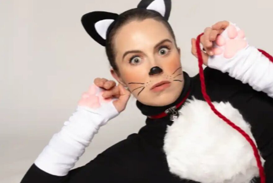Woman wearing a cat suit with ears and whiskers, holding a red cord.