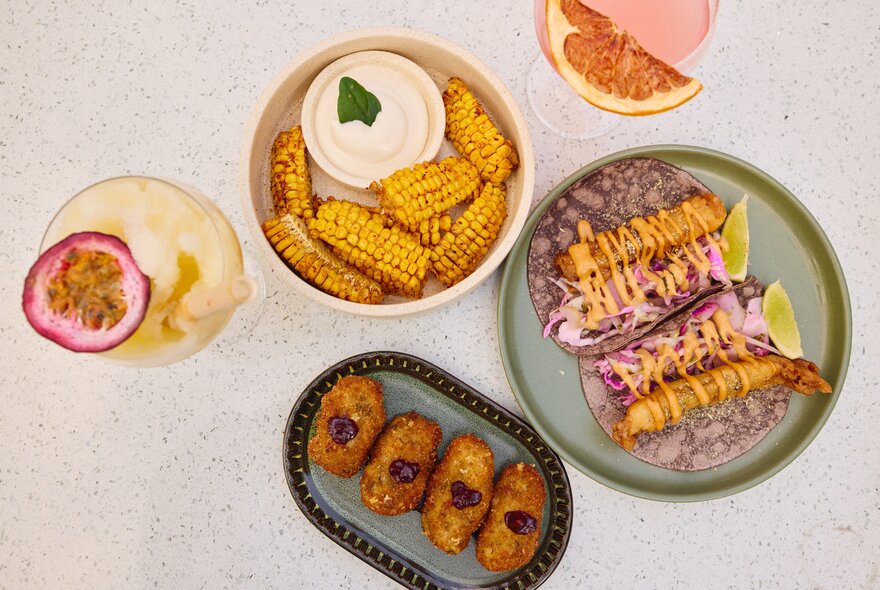 A table set with Mexican fishes including corn, tacos and margaritas.
