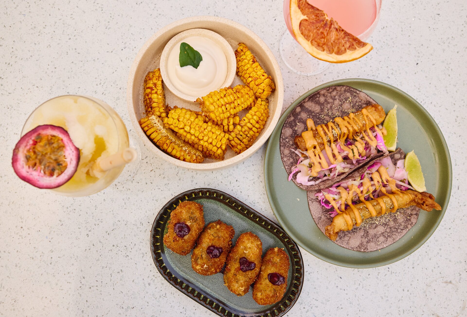 A table set with Mexican fishes including corn, tacos and margaritas.