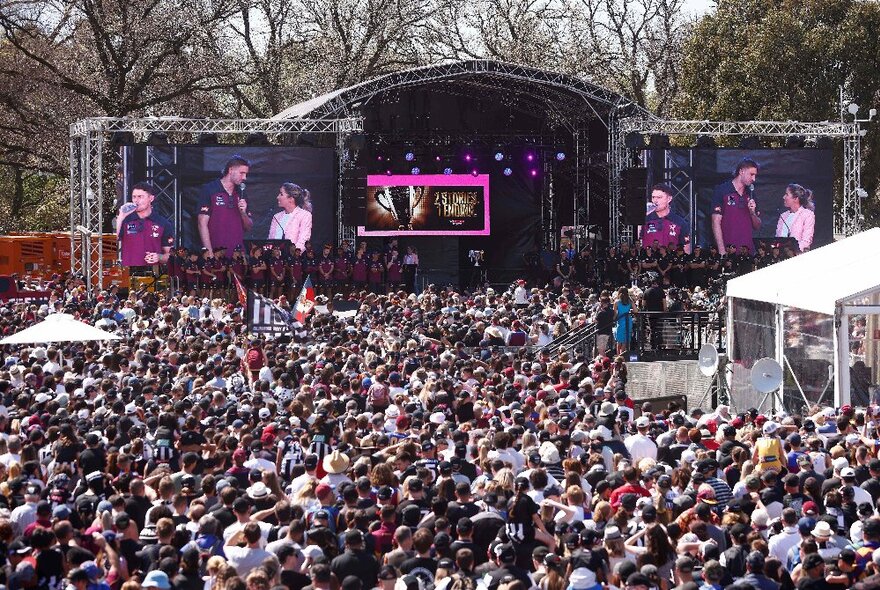 A huge crowd of people and a stage with large screens televising interviews. 