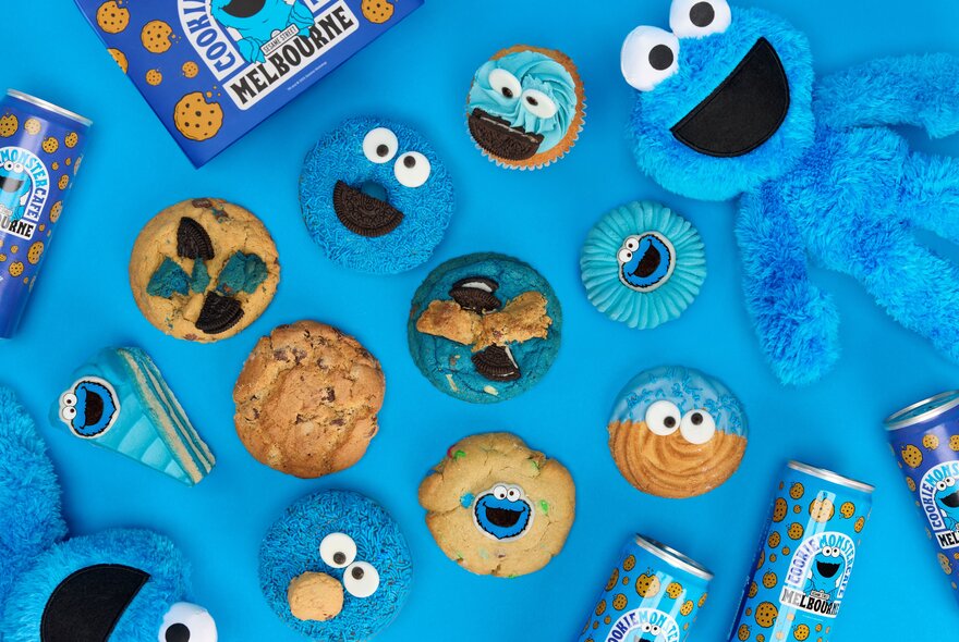 Overhead view of Sesame Street and Cookie Monster themed cookies and cakes displayed on a blue table.