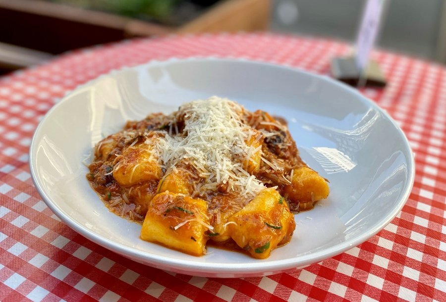 Bowl of gnocchi in a Napoli sauce with parmesan on a table with a red and white checked table cloth.