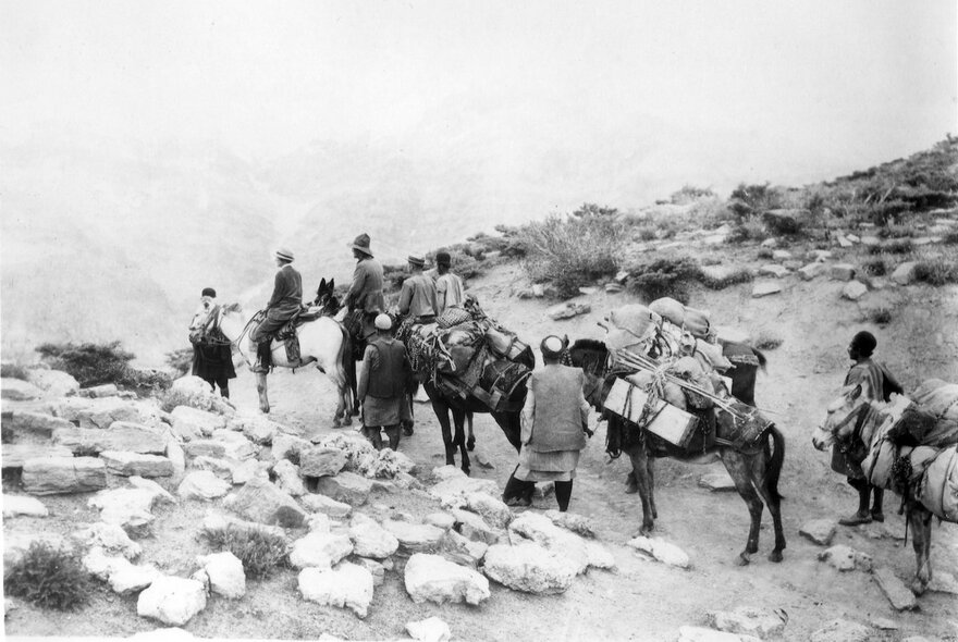 A still from a black and white movie about Iran, showing people on horses in a rocky terrain. 