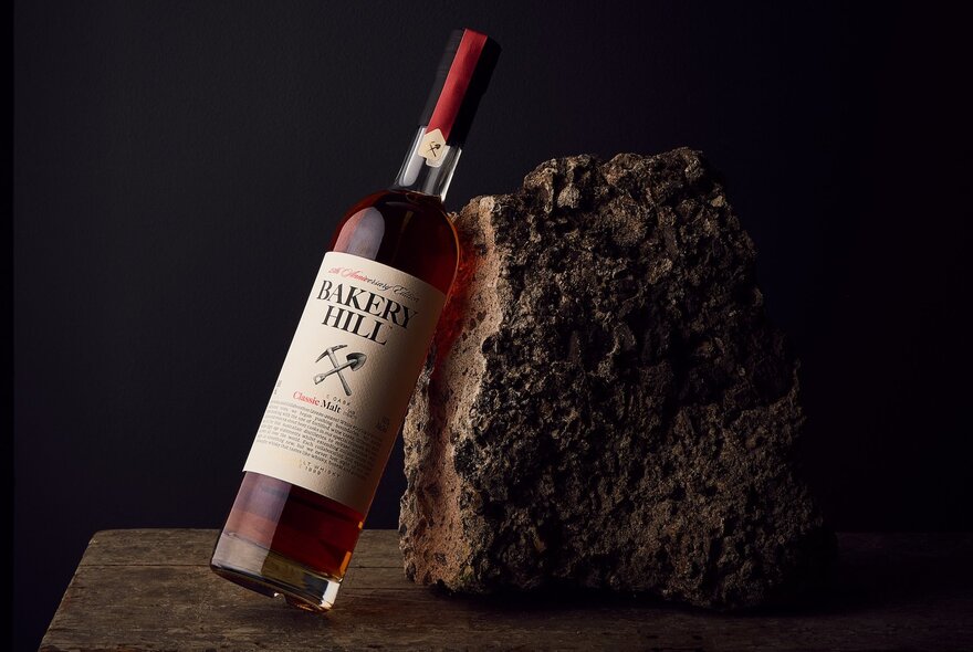 A bottle of Bakery Hill whisky on display leaning against a large piece of rock.