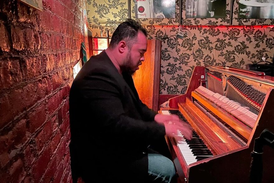 Musician Umar Zakaria in profile playing a piano in a small club.