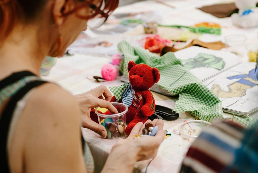 Person making teddy bear artwork with beads and fabric.