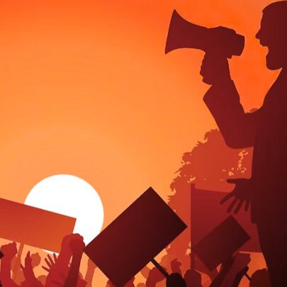 Man speaking into a loud hailer while people wave placards against a setting sun.