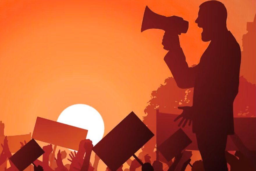 Man speaking into a loud hailer while people wave placards against a setting sun.