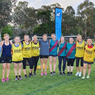 Team of women standing arm in arm on a sporting field with trees in the background.