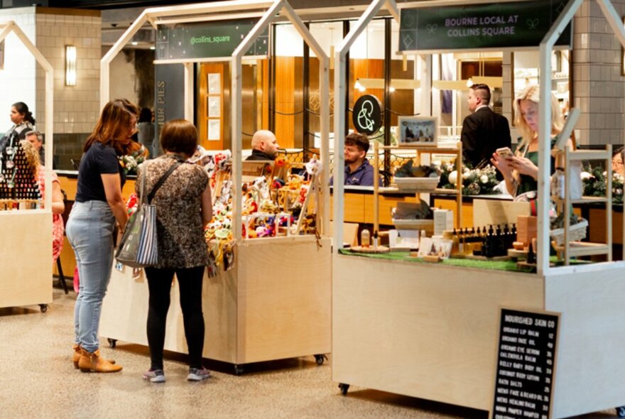 People wandering around a indoor plaza browsing craft market stalls.