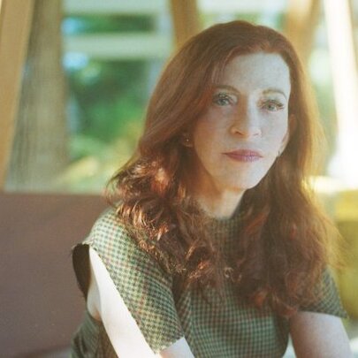 Author Susan Orlean with long red hair, seated in a sunny room with windows.