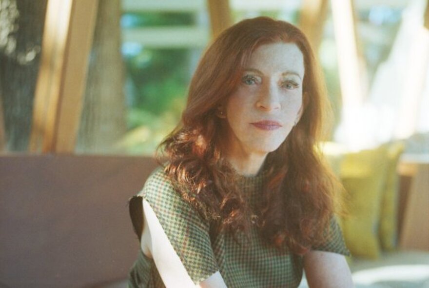 Author Susan Orlean with long red hair, seated in a sunny room with windows.
