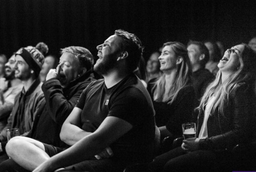 Two rows of seated people laughing and holding drinks. 