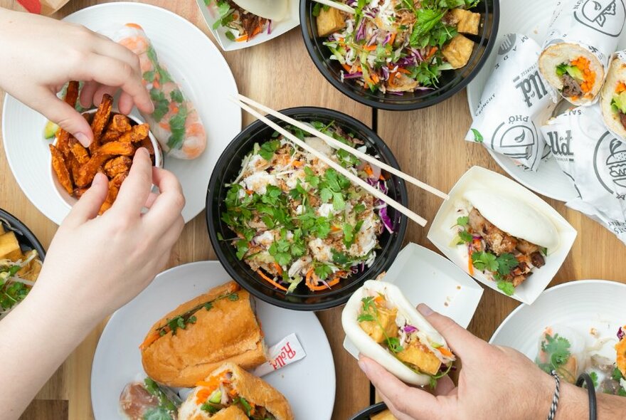 Table spread with food including bao, bahn mi and noodle dishes.