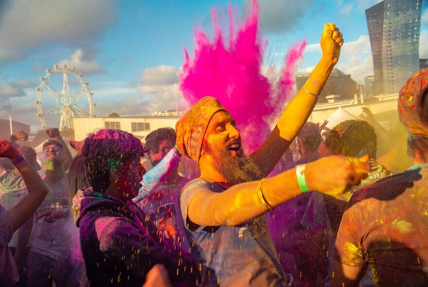 People dancing and celebrating Holi festival, a pink colour bomb going off in the background. 