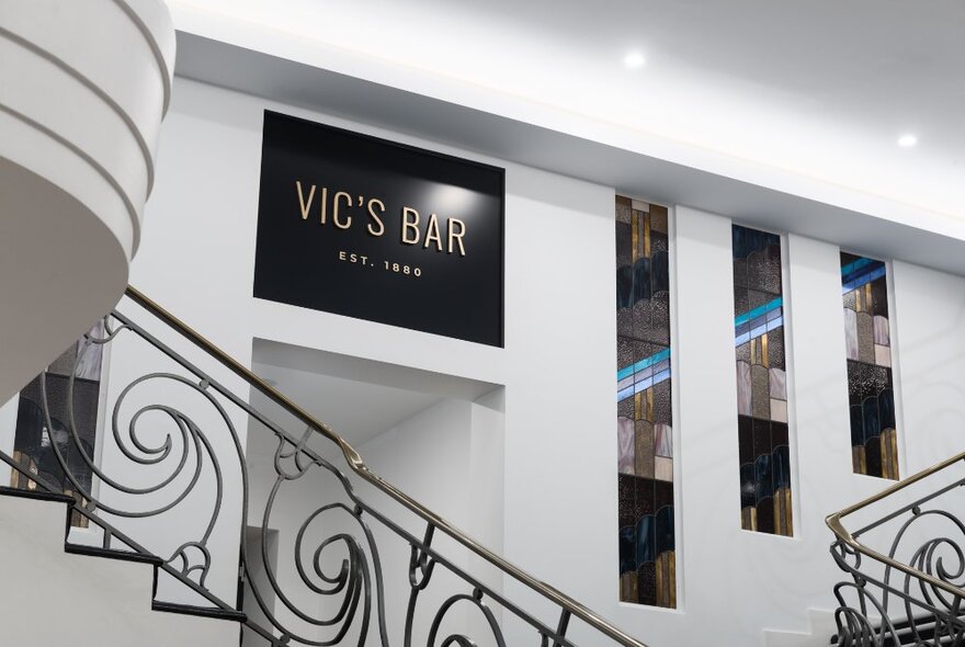 The interior of Vic's Bar in Melbourne, with white walls and an ornate iron ballustrade on a white staircase.