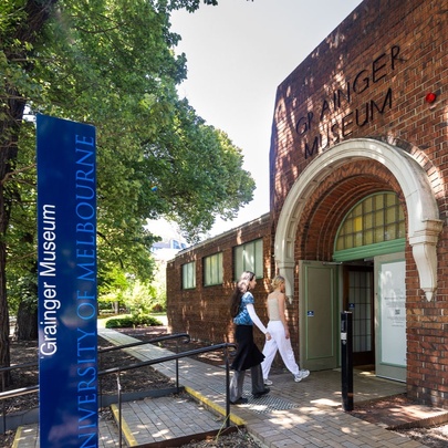 People entering the museum arched entrance under leafy trees.