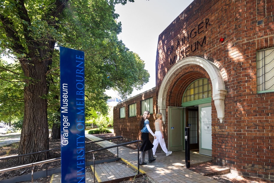 People entering the museum arched entrance under leafy trees.