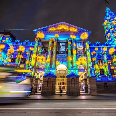The facade of Melbourne Town Hall illuminated in colours, with a blurred tram going past.