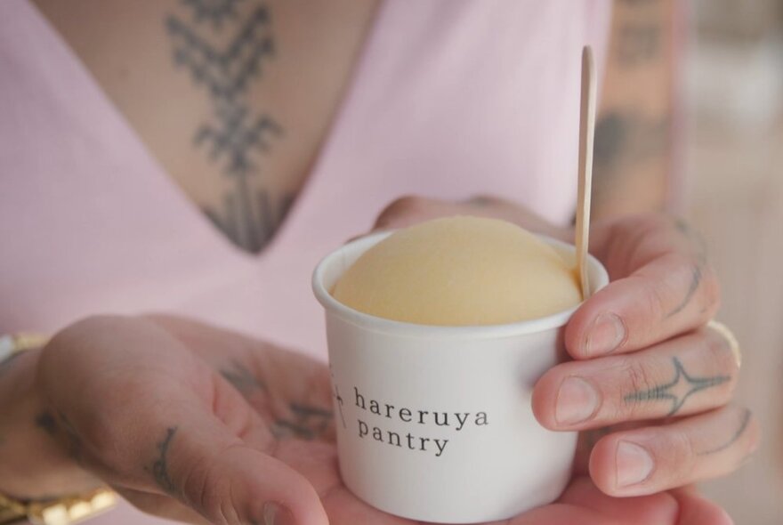 A cup of mochi wrapped ice cream held by a women with tattoos.