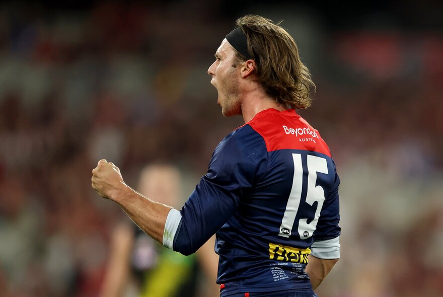 A Melbourne AFL player cheering himself on with pumped fists, on the footy field.