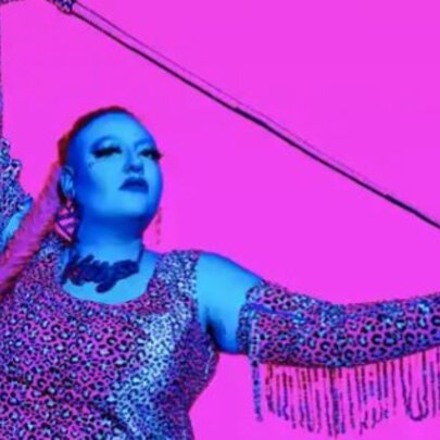 Burlesque performer wearing a glittery tank top with long fringed gloves, holding a wire.