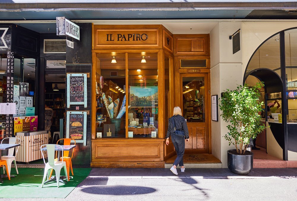 A blonde woman walking into a narrow store with an old-fashioned timber exterior. 