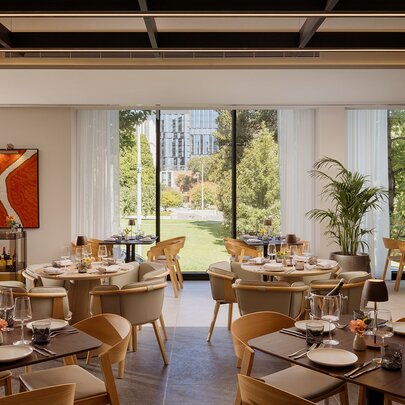 Modern restaurant dining room at Fico, with tables and chairs next to large glass windows and view onto gardens.