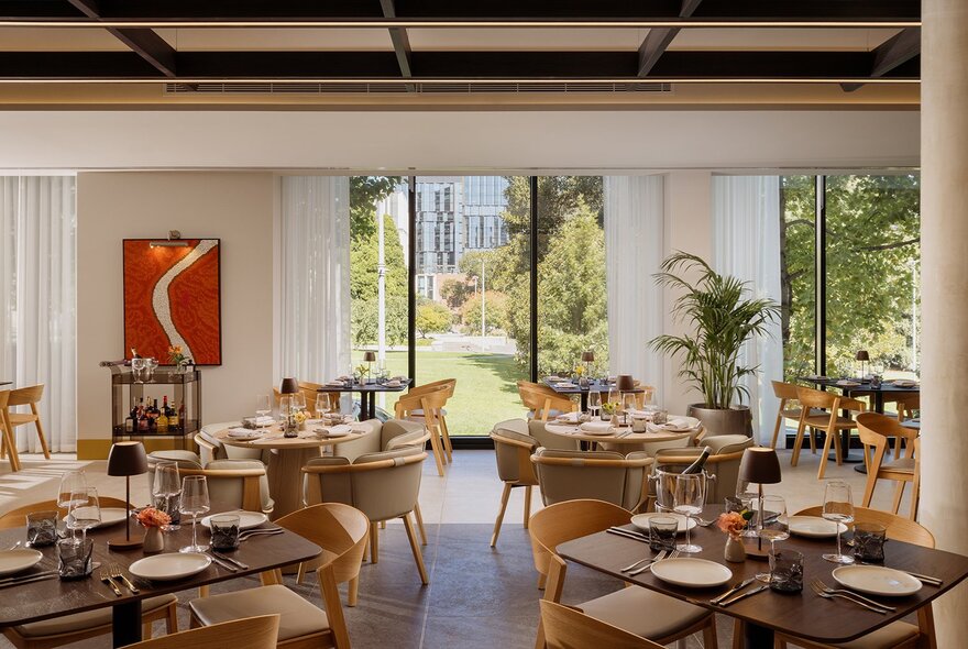 Modern restaurant dining room at Fico, with tables and chairs next to large glass windows and view onto gardens.