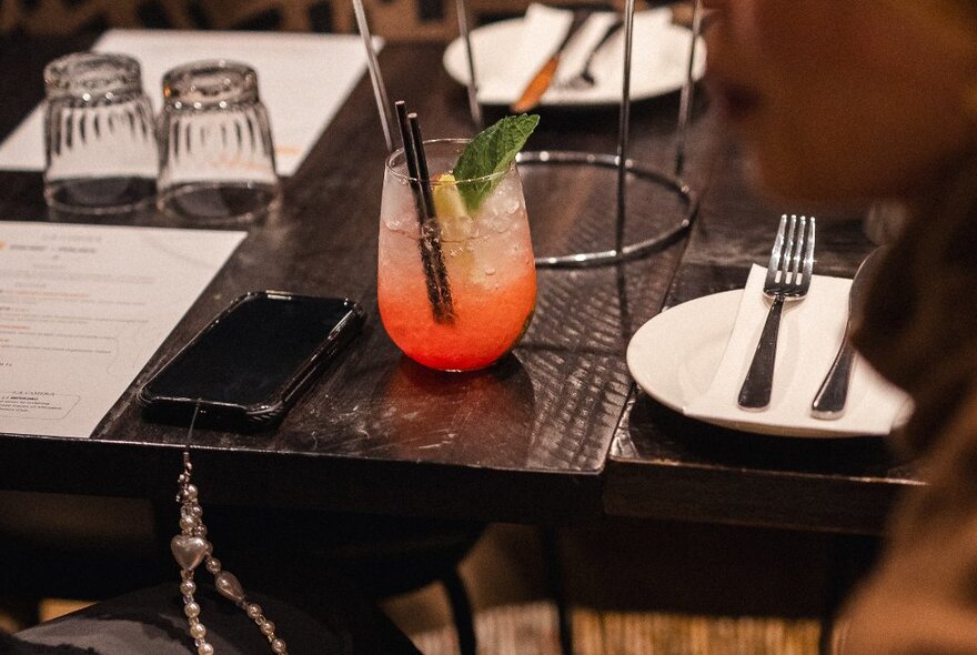 A dark table set for dinner with an iced cocktail.