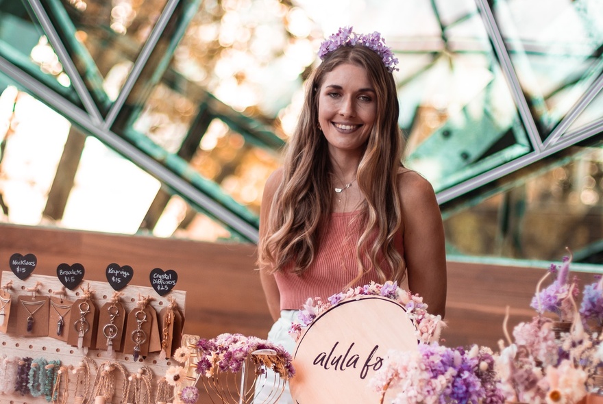 A stallholder wearing a floral headdress standing in front of a crafts stall.