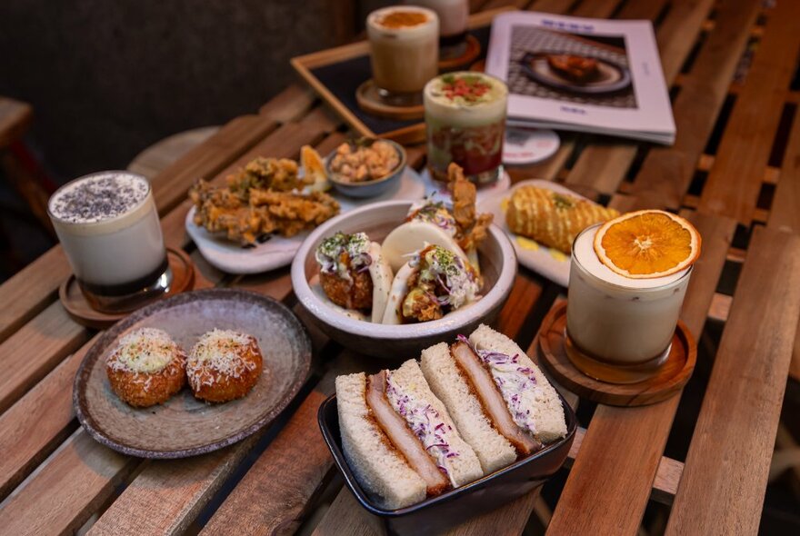 Wooden table with plates of Japanese food and frothy drinks.