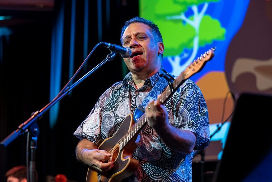 Singer-songwriter David Ardern performing on stage, playing guitar and singing into a microphone.