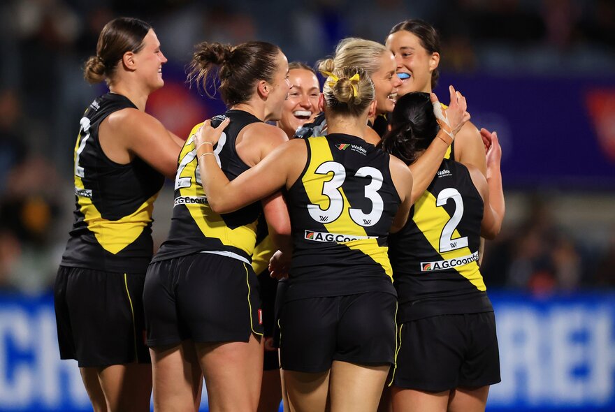 Richmond AFLW players celebrate in a huddle. 