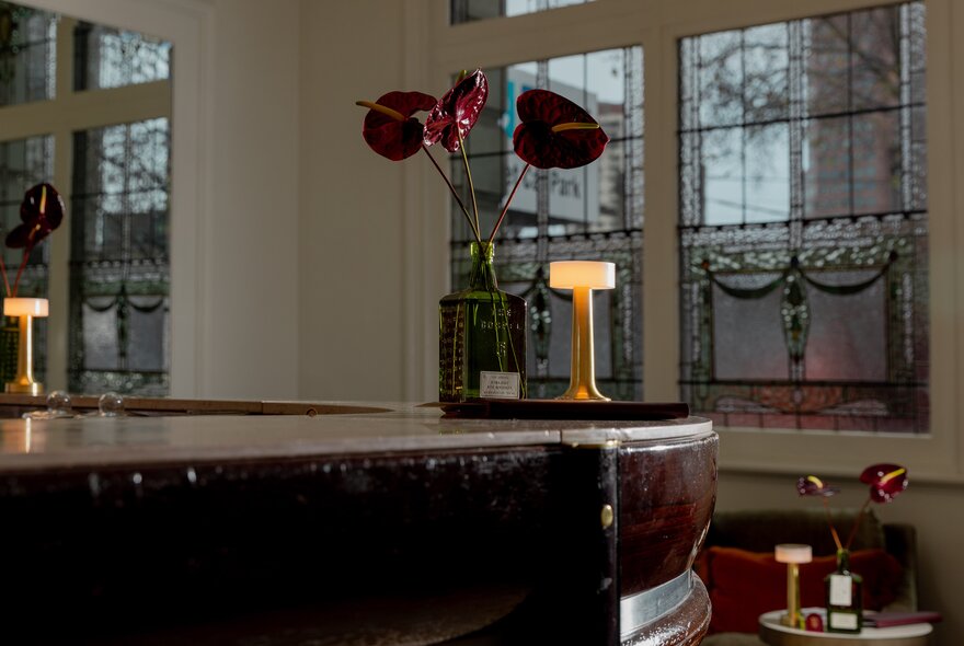 The interior of a bar with ornate windows, table lamps and a vase of flowers. 