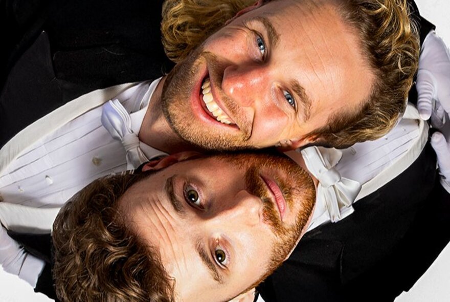 Two bearded men wearing tuxedos, looking upwards, one upside down.