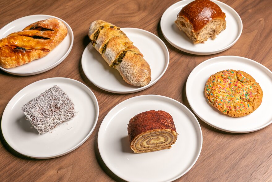 A selection of savoury and sweet food  items on white plates on a wooden counter.