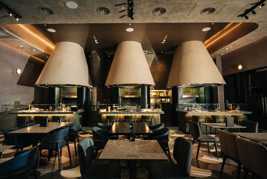 Dining space with dark tables and chairs under oversized overhead lamps, brown and beige decor.