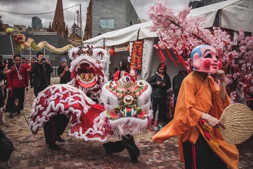 An outdoor Lion Dance performance, with people dressed in lion puppet costumes, and carrying fans and decorations.