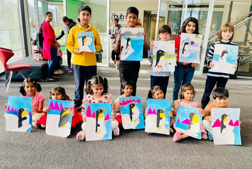 A standing and seated row of children in a room, all holding up artworks they've created.