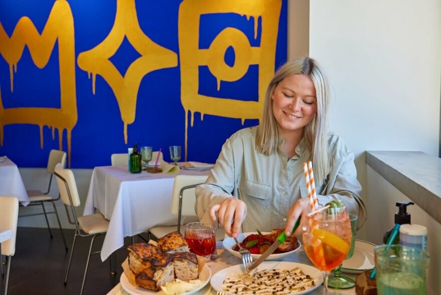 A woman sitting at a restaurant cutting in to a pizza.