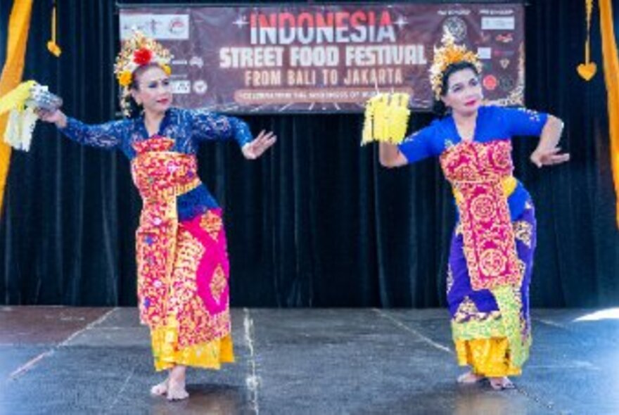 Two dancers in traditional colourful costumes performing a cultural dance on a stage at the Indonesian Street Food Festival.