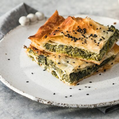 Two slices of flaky Greek spanakopita on a white plate.
