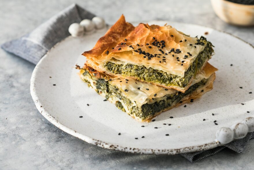 Two slices of flaky Greek spanakopita on a white plate.