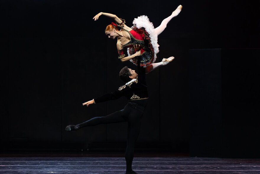 Dramatically lit ballet dancers performing mid-poise with arms and legs stretched.