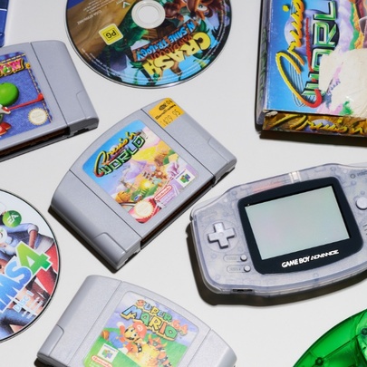 Top down view of a collection of classic retro video games and consoles, including a Nintendo Game Boy Advance handheld system and several Nintendo 64 cartridges.