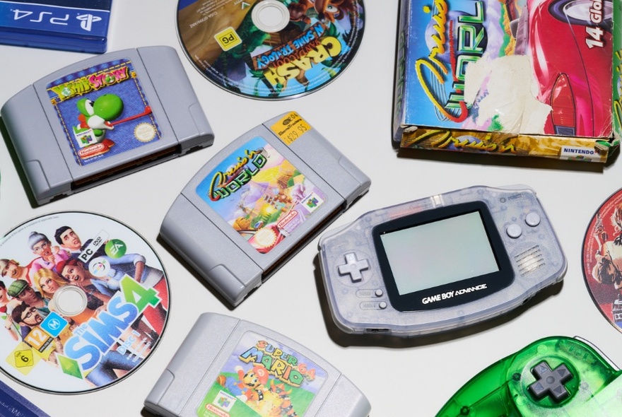 Top down view of a collection of classic retro video games and consoles, including a Nintendo Game Boy Advance handheld system and several Nintendo 64 cartridges.
