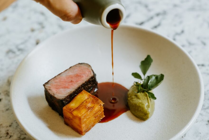Sauce being poured from a small jug onto a plate of food. 