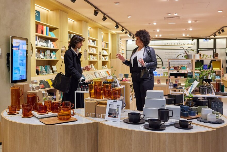 Two people browsing in a shop next to display of glass and ceramic coffee cups.