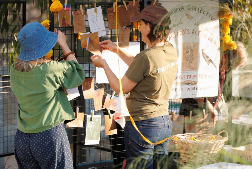 People hanging items on a trellis with pegs in a market stall setting.